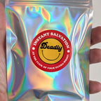 A hand holding a silver holographic pouch with a circular red and yellow label that reads 'Instant Salvation' and 'Deadly'.