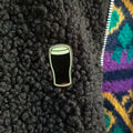 Pin of a pint glass on a textured black surface with a colorful patterned fabric background.