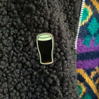 Pin of a pint glass on a textured black surface with a colorful patterned fabric background.