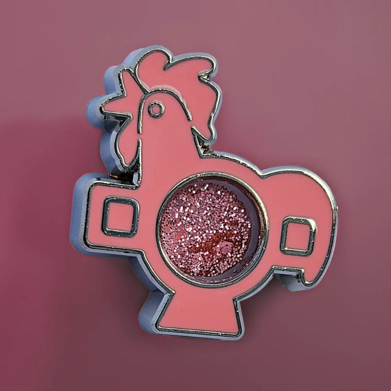 Pink rooster-shaped enamel pin with glittery center on a pink background
