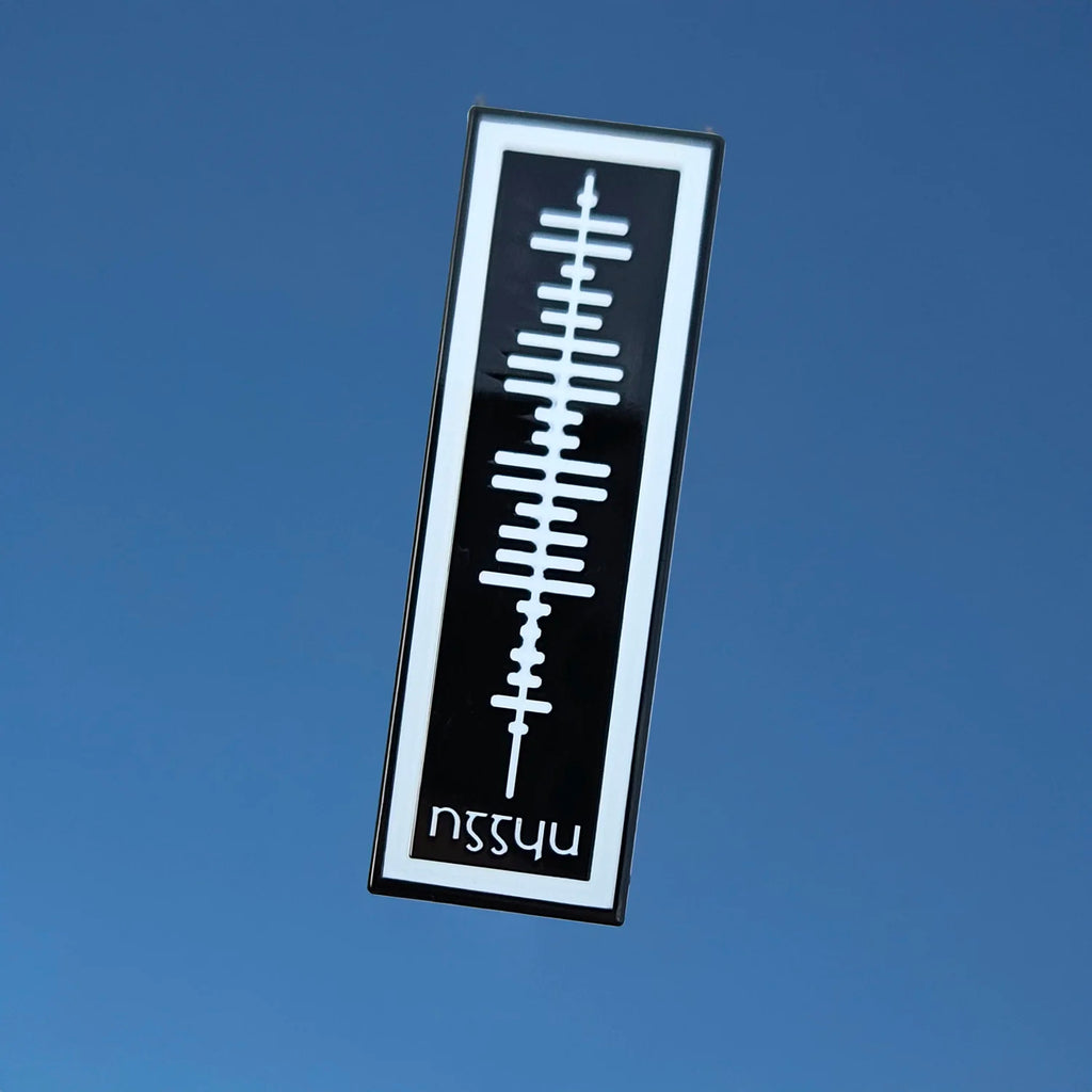 Ogham in white on a black enamel pin against a blue background