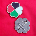 Colorful heart-shaped Palestine brooch and a silver brooch with engraved text on a pink background