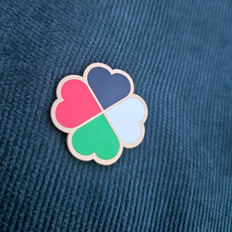 Four-heart clover-shaped pin on a textured blue fabric background
