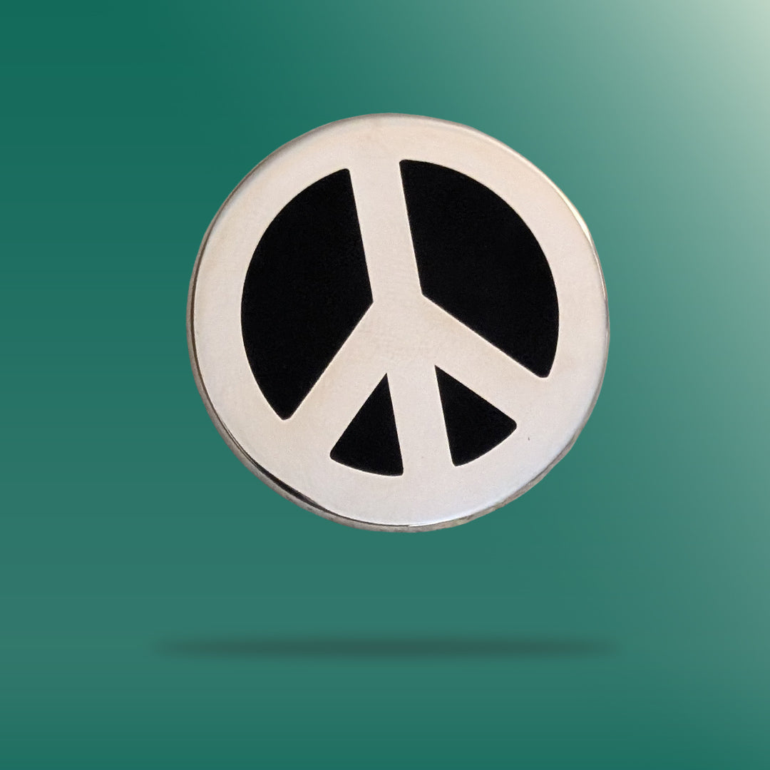 A silver peace sign pin badge against a gree background