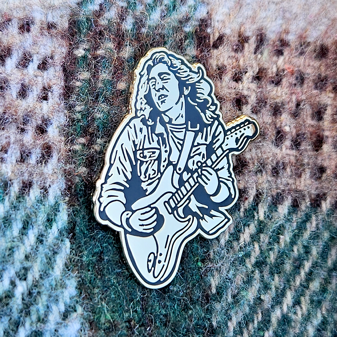 Enamel pin of Rory Gallagher playing guitar on a textured fabric background