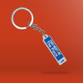 a blue and white keyring in the style of a Dublin Street sign that reads 'this must be the place'. It is against an orange background