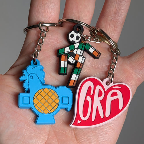 Three keyrings being held to show scale. The keyrings are blue and yellow, green, white and orange, and red and pink,