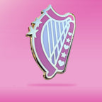 A pink harp-shaped enamel pin with stars and hearts on a pink background
